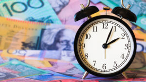 An alarm clock reading 2:04 sits with a background of blurred Australian money
